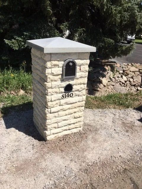 Stone mailbox with a dark metal mail slot and address numbers, under a gray concrete top.
