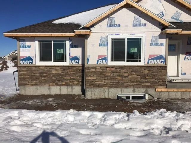 House under construction with stone veneer siding, two windows, and snow on the ground.