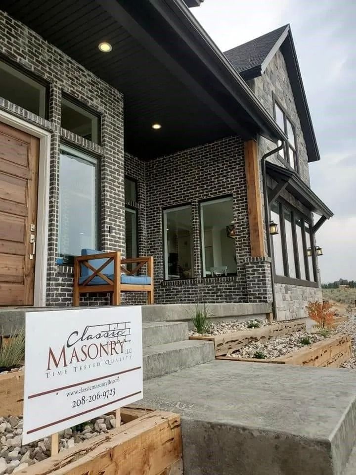 Modern brick house with a sign for Classic Masonry. Grey and black brick with a wooden door and porch.