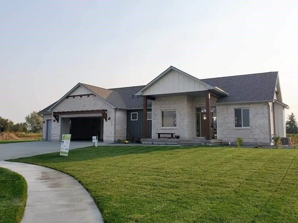 A modern, single-story house with a light brick exterior and a dark gray roof, a green lawn, and a curved sidewalk.