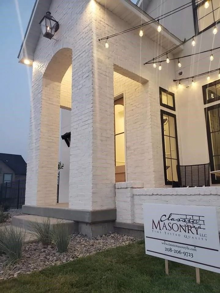 White brick house with arched entryway, string lights, sign on lawn.
