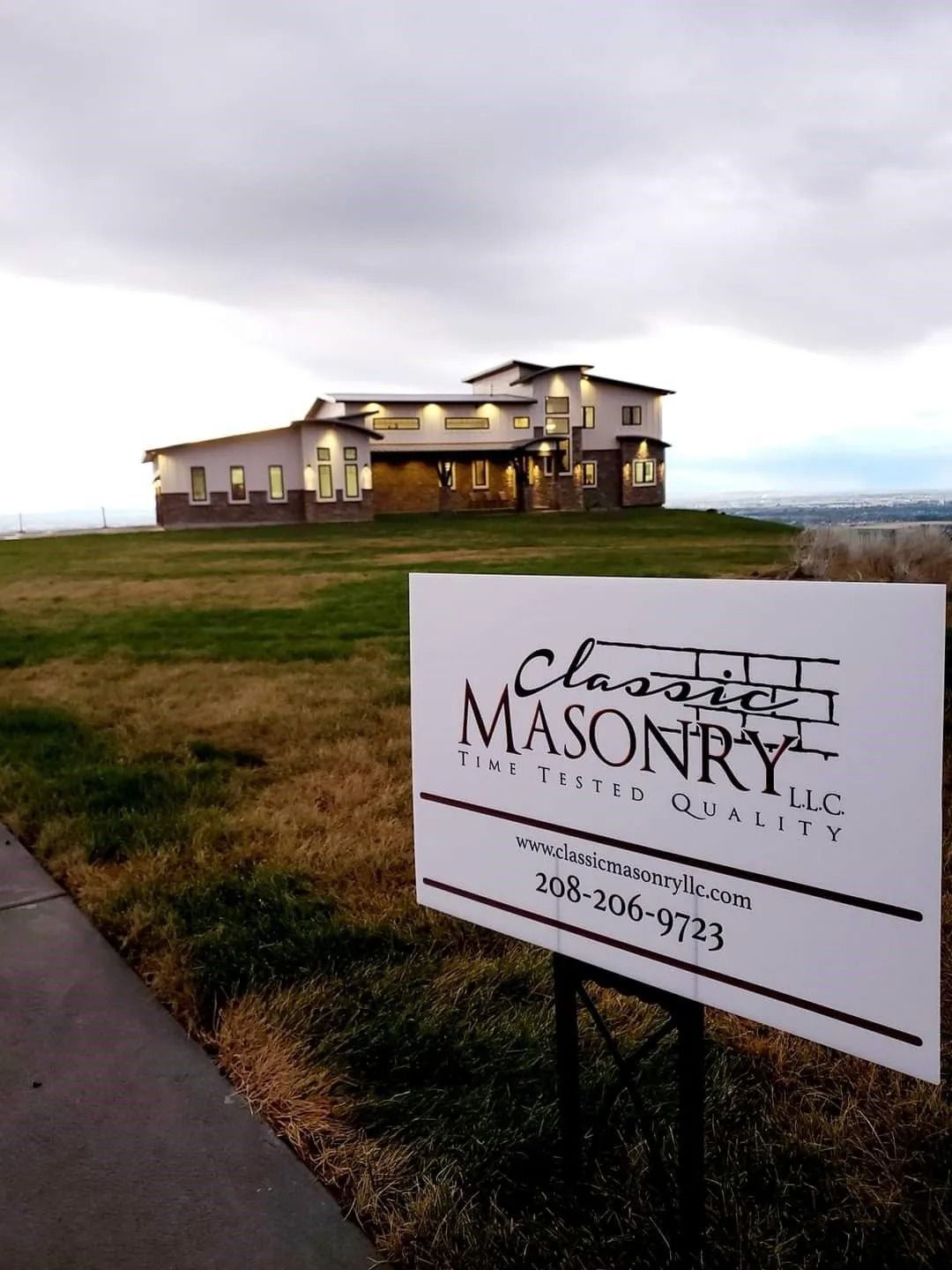 Sign for Classic Masonry in front of a modern house on a hill, with an overcast sky.