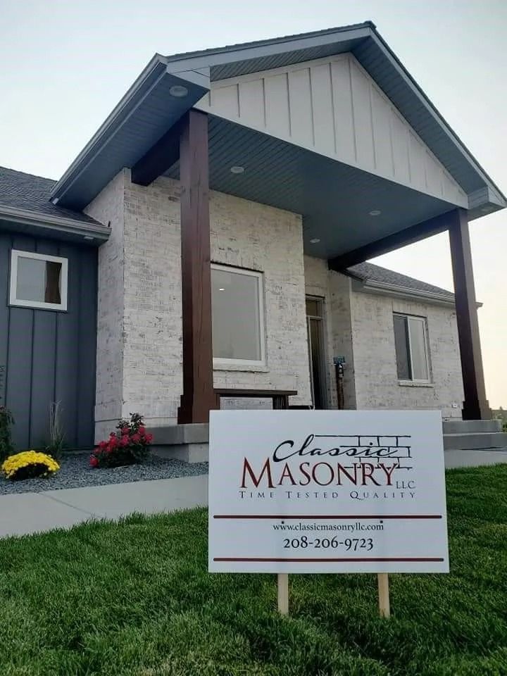 A house with light brick siding and dark brown porch columns; a sign for Classic Masonry in front.