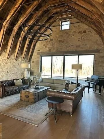 Living room with stone walls, wooden vaulted ceiling, leather sofas, large window, piano.