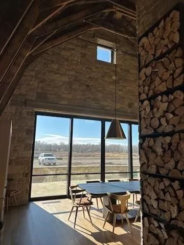 Dining room with large windows, wood-stacked wall, and a view of a road and sky.