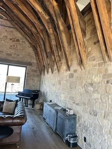 Interior of a room with stone walls, arched wooden beams, a piano, and a leather sofa.