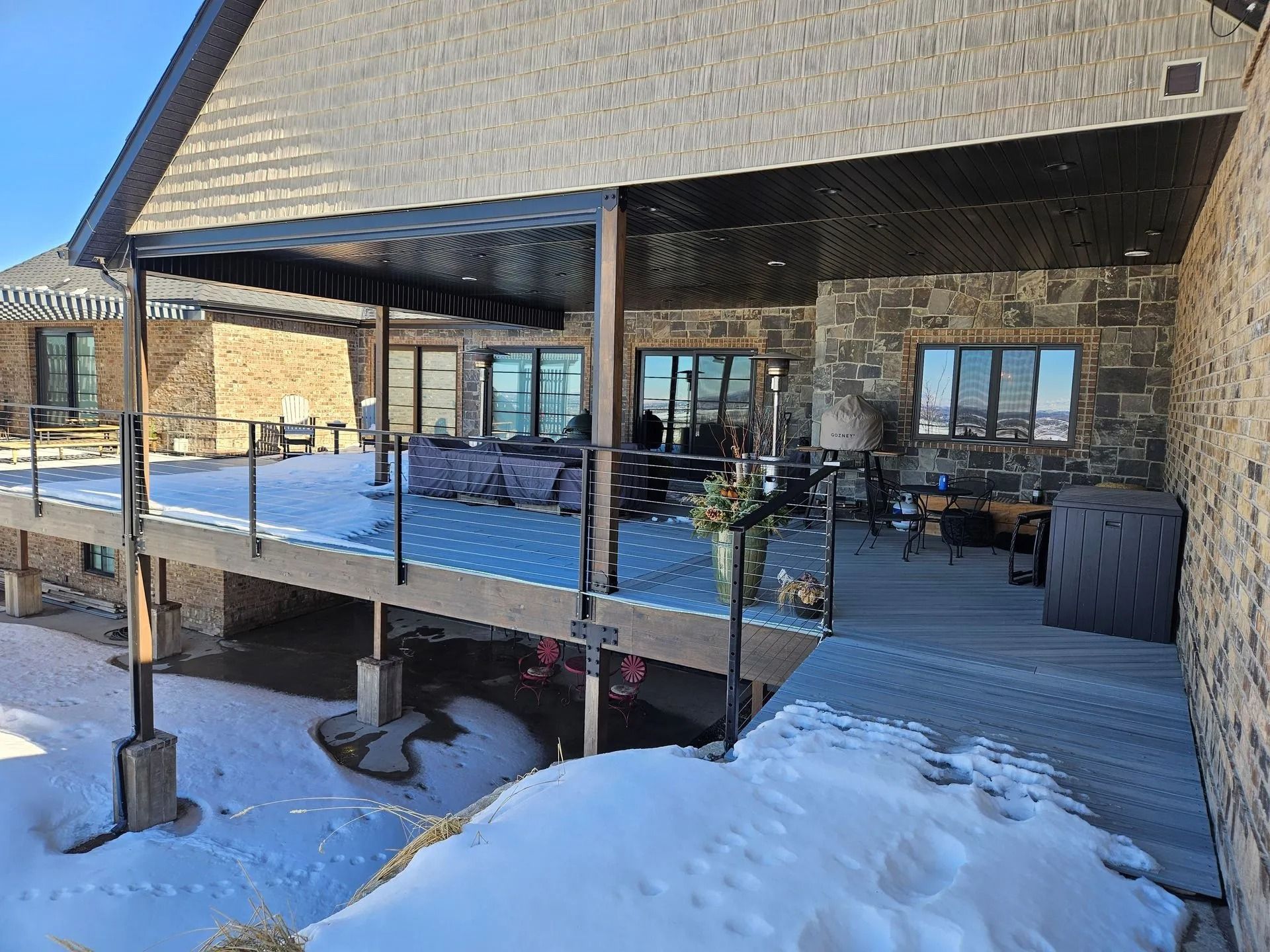 A snow-covered deck with a covered seating area attached to a stone-clad building.