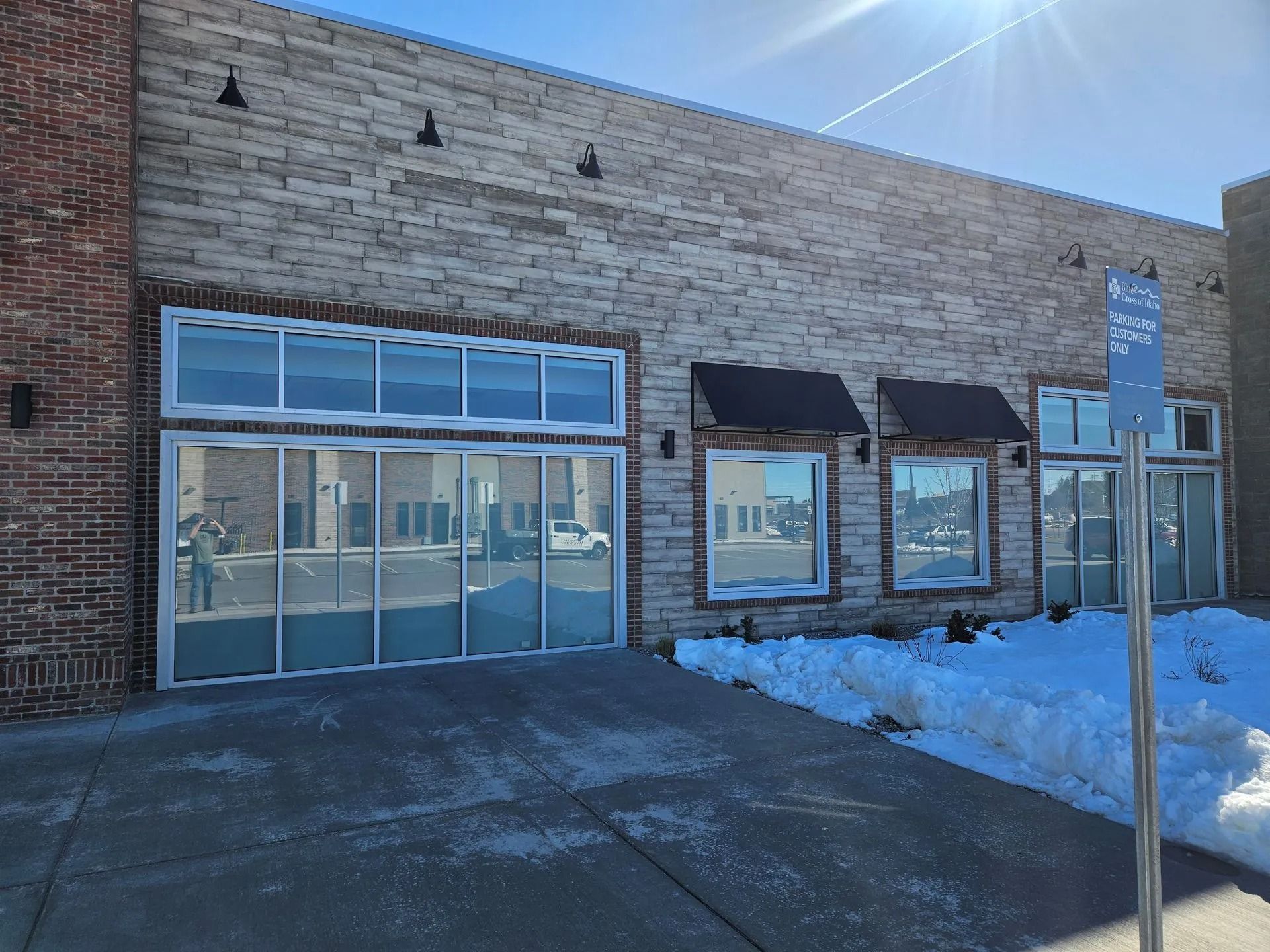 Brick building with large windows and a snowy sidewalk.
