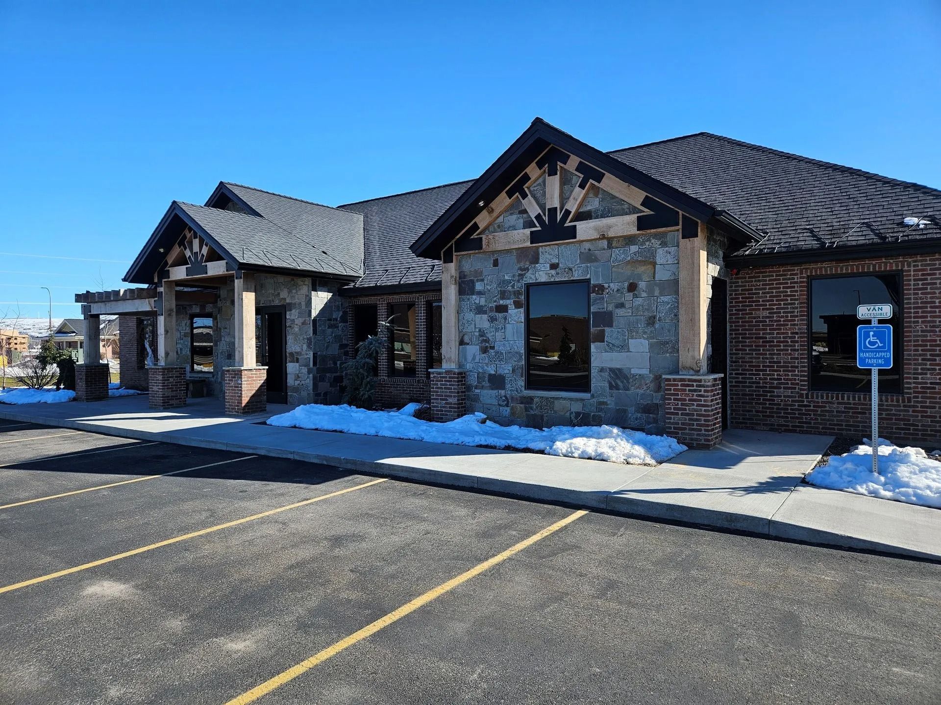 Stone and brick building with dark roof, accessible parking, and patches of snow.