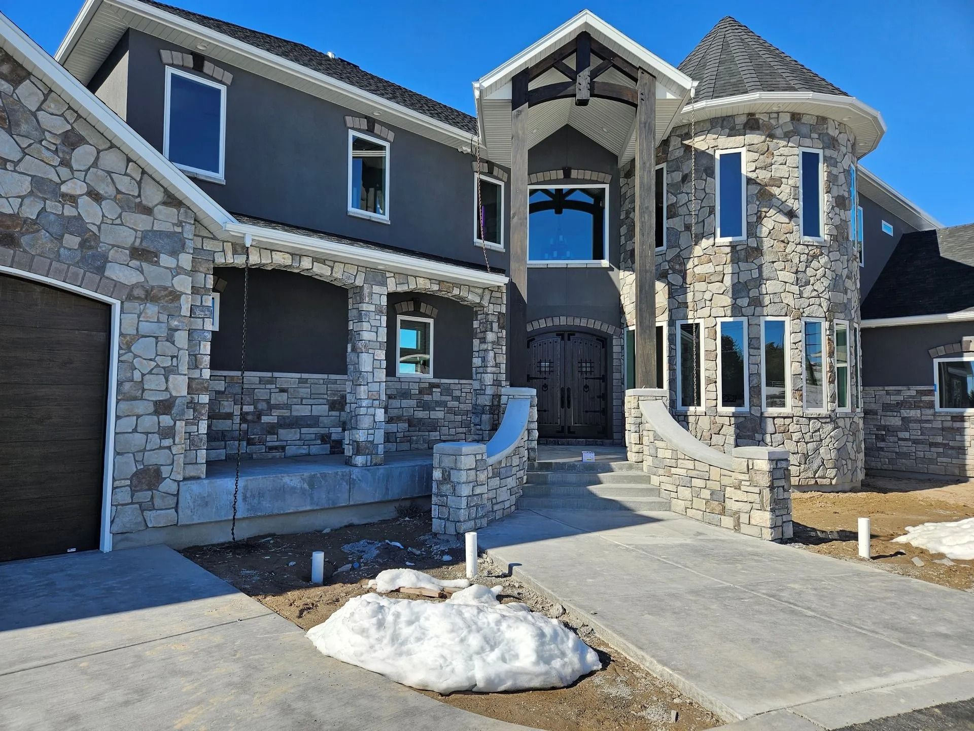 Two-story house with stone facade, arched entry, circular tower, and concrete driveway.
