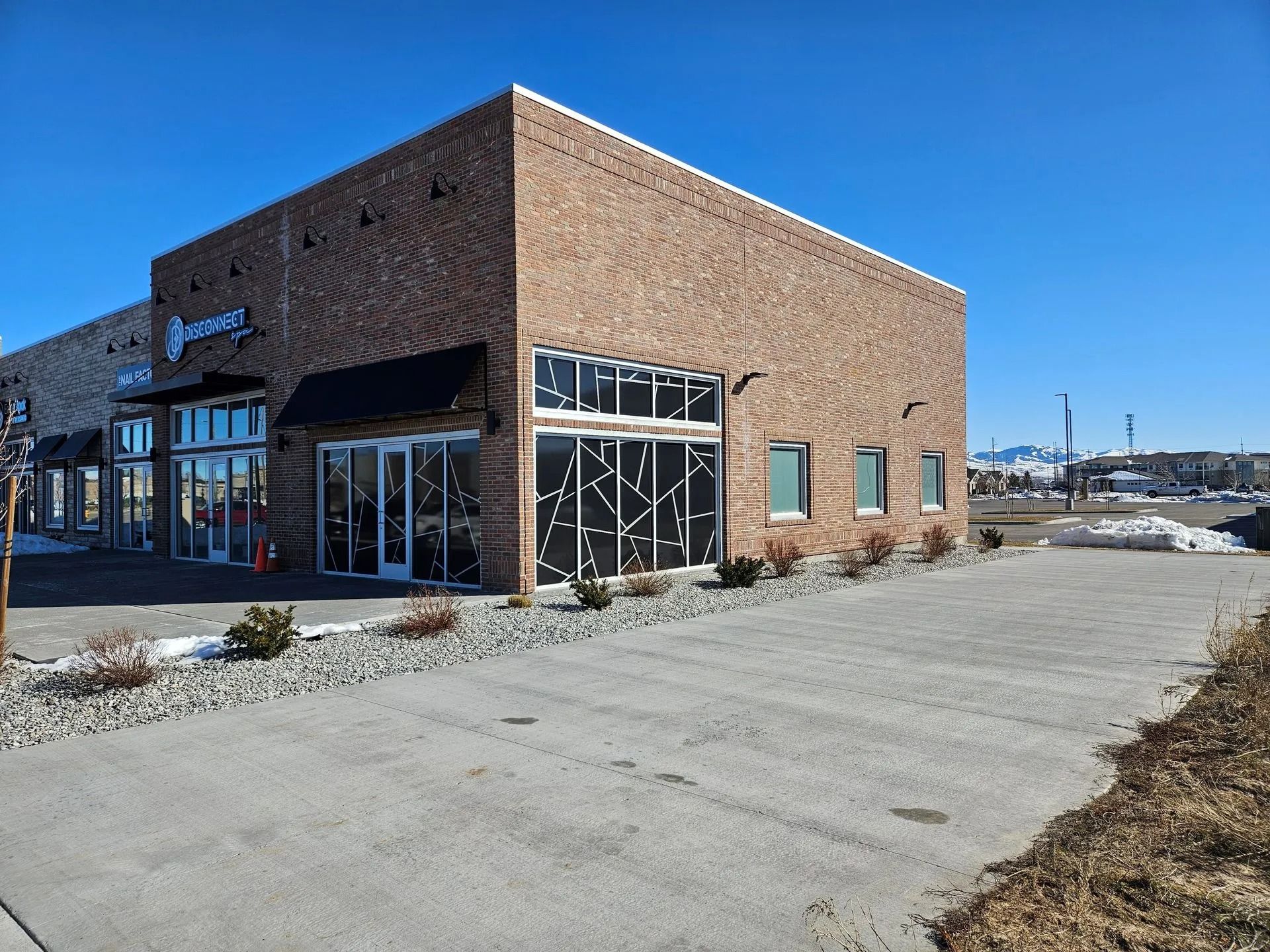 Brick building with large windows and a black awning on a sunny day.