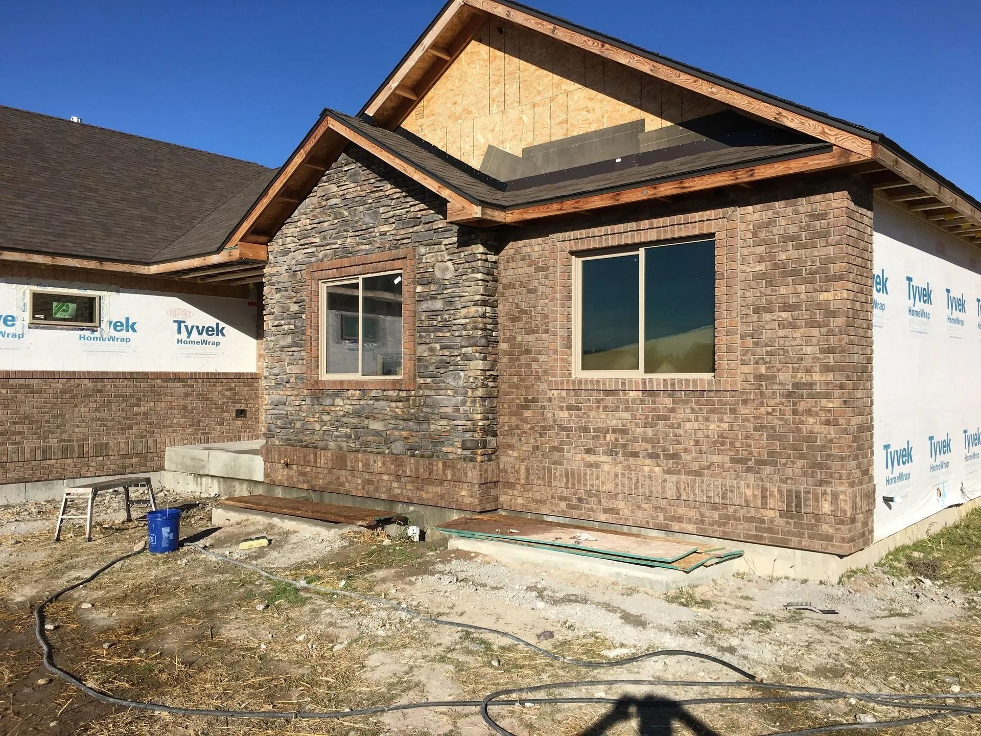 Exterior of a house under construction; brick and stone facade, windows, and exposed framing.