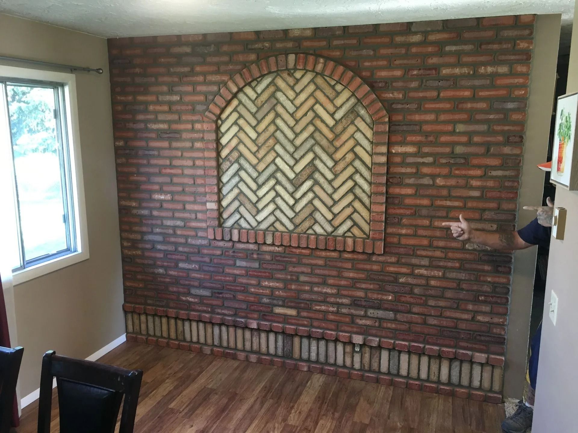 Brick accent wall with arched herringbone design, beside a window and wooden floors.