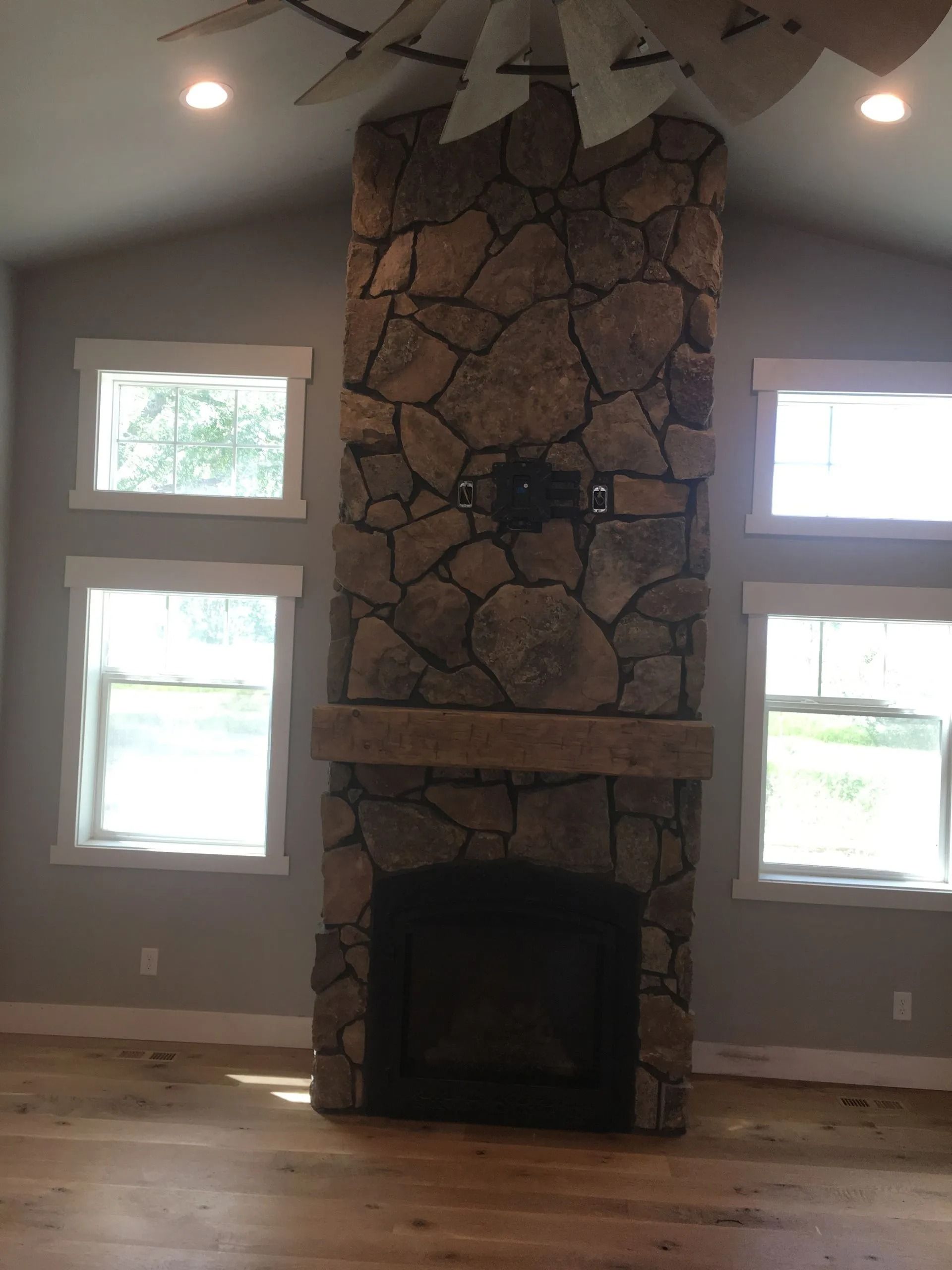 Stone fireplace with a wooden beam, flanked by windows.