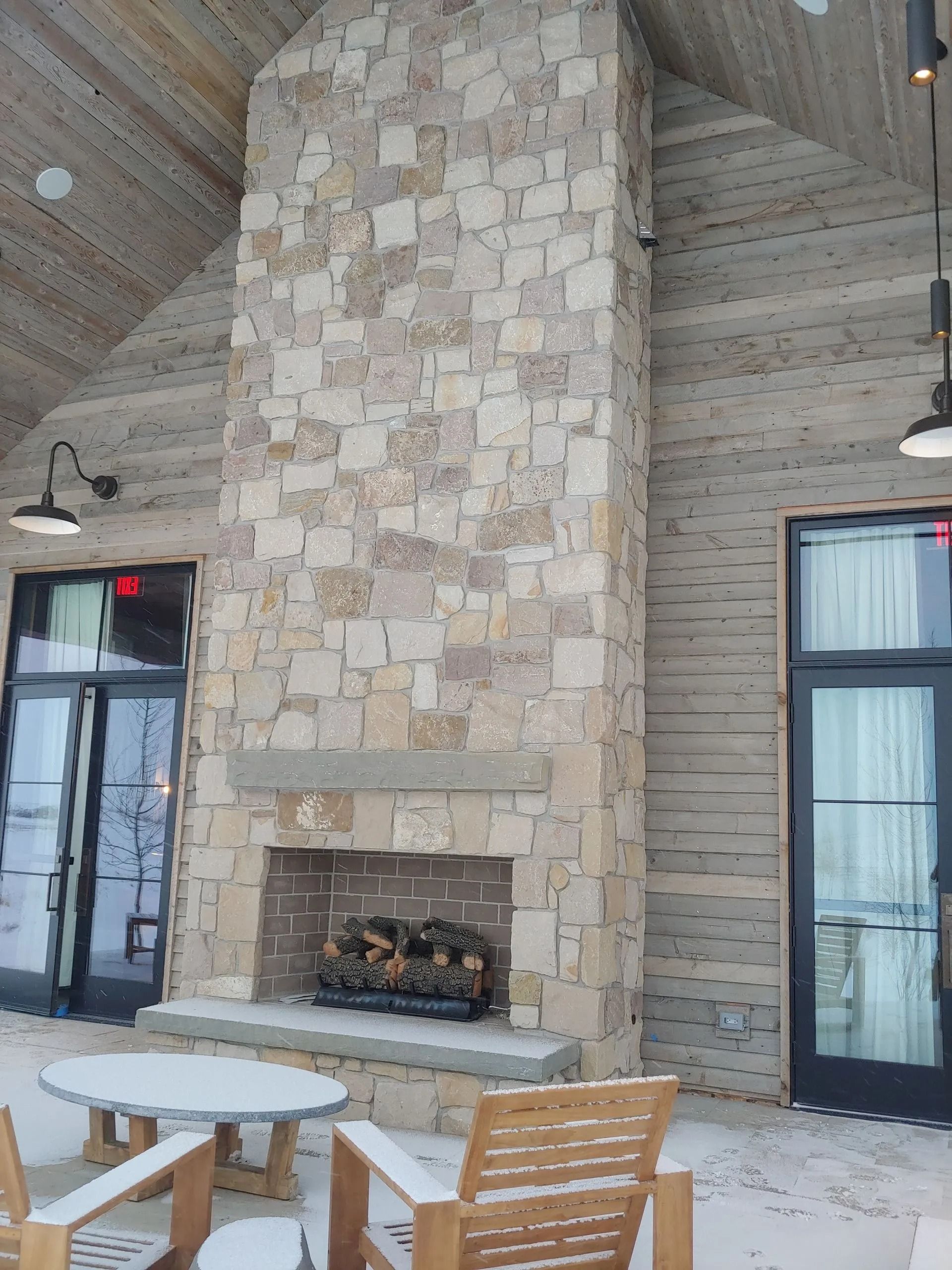 Stone fireplace with wood burning inside. Flanked by doors and under a slatted ceiling.