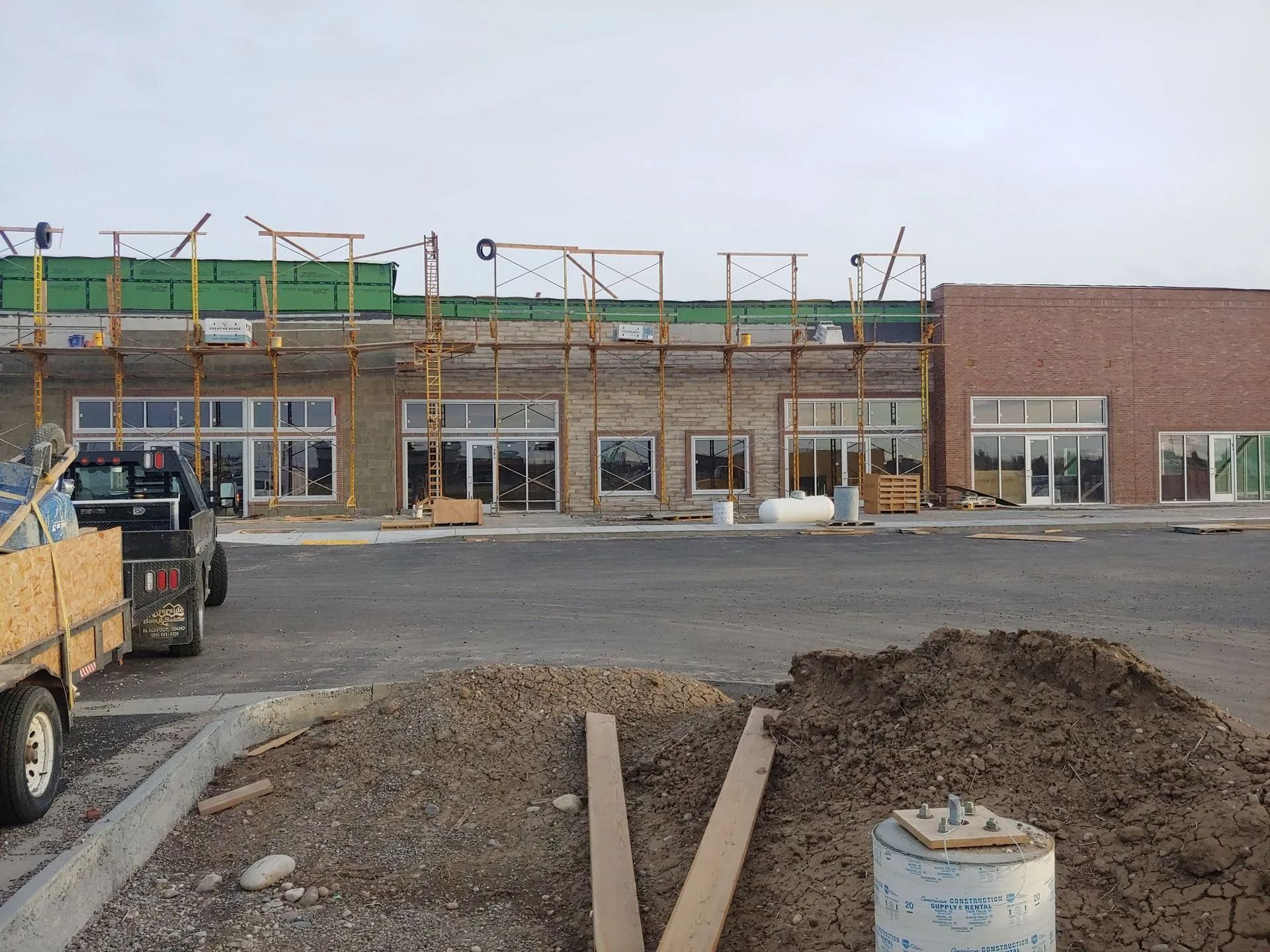 Building under construction with scaffolding, windows, and dirt pile in the foreground, cloudy sky.