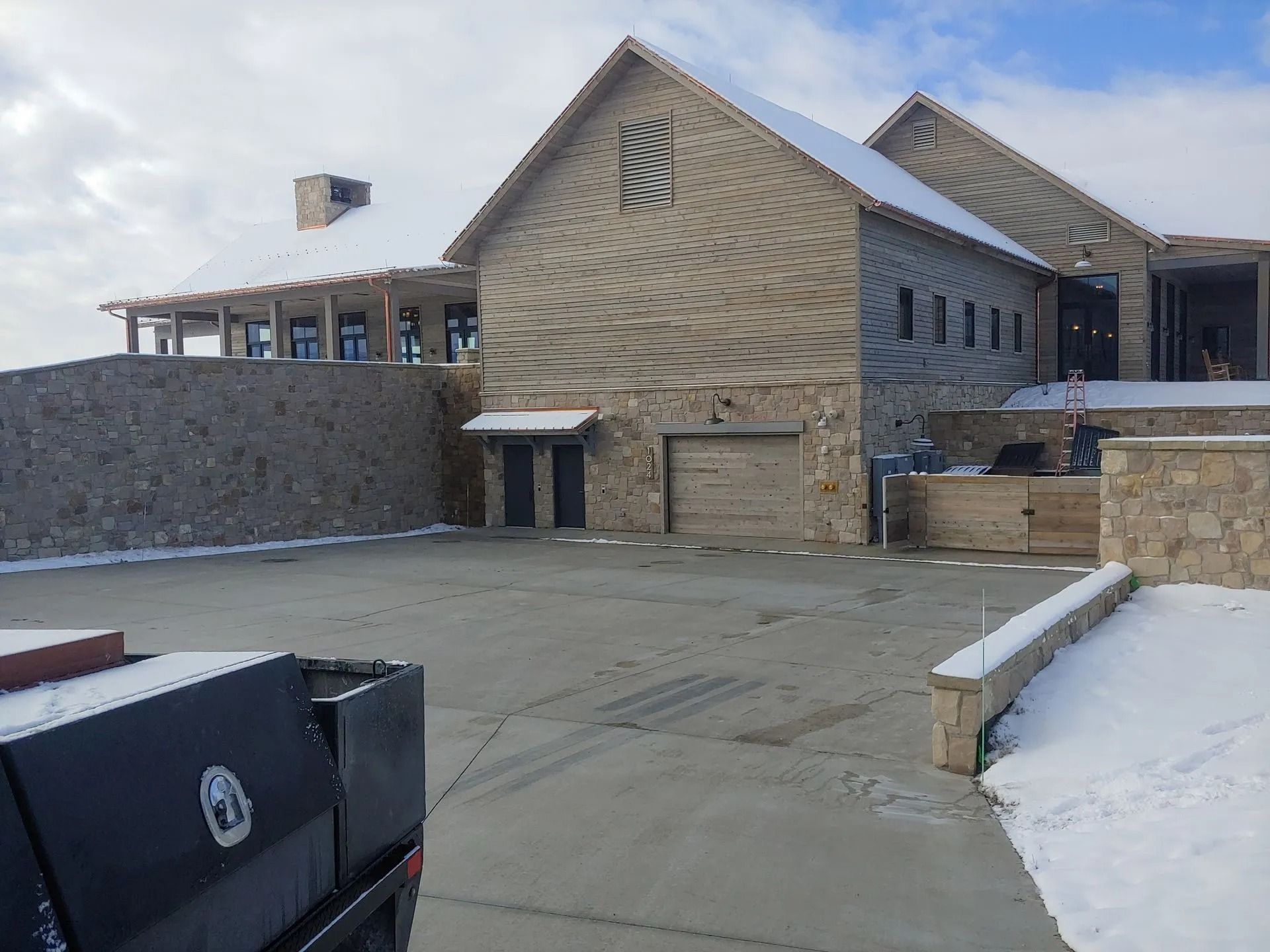 A large stone house with a snow-covered roof, driveway, and walls. A truck is parked in the foreground.