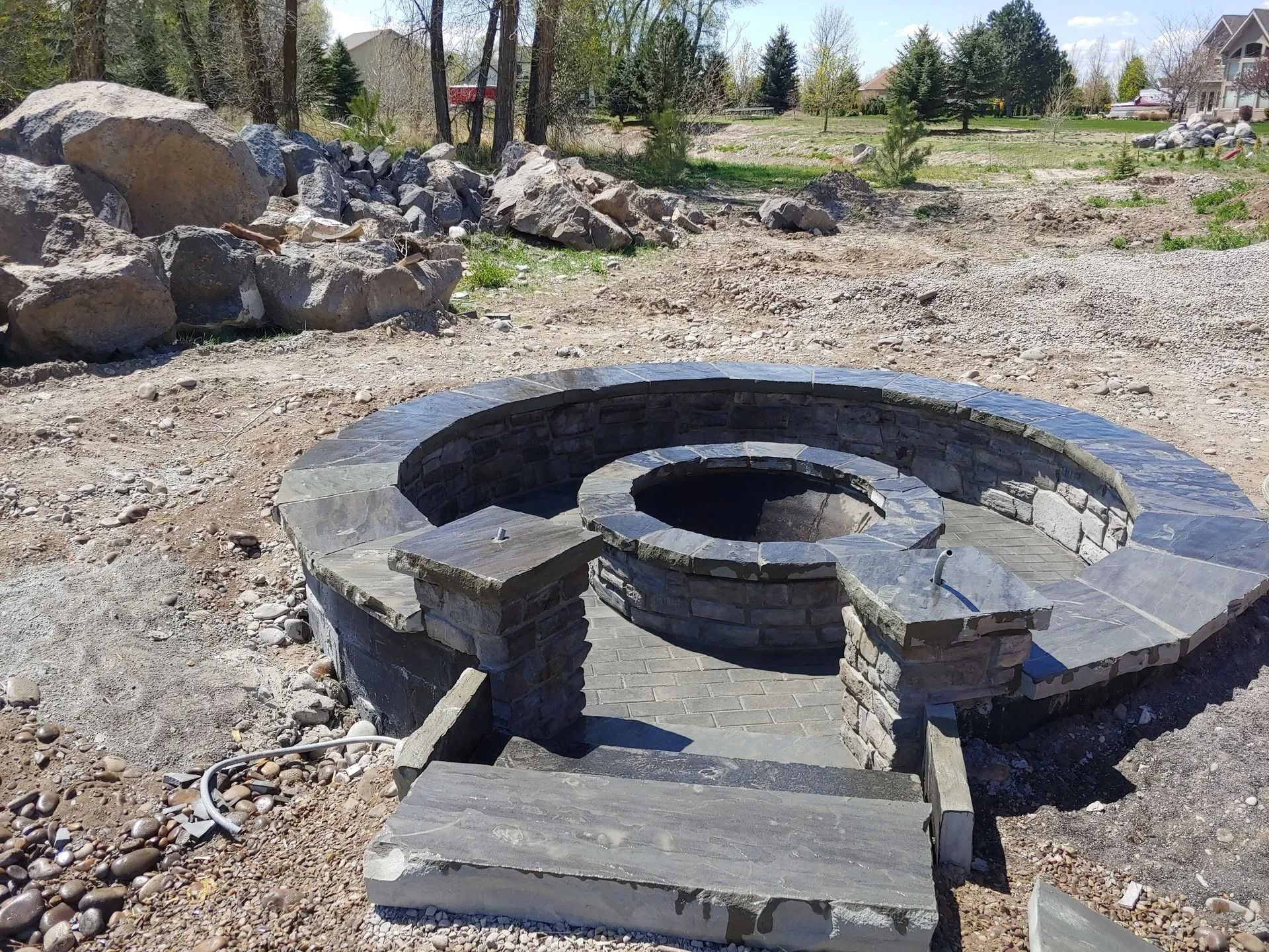 Stone fire pit under construction in a yard. Grey stone steps lead up to a circular structure.