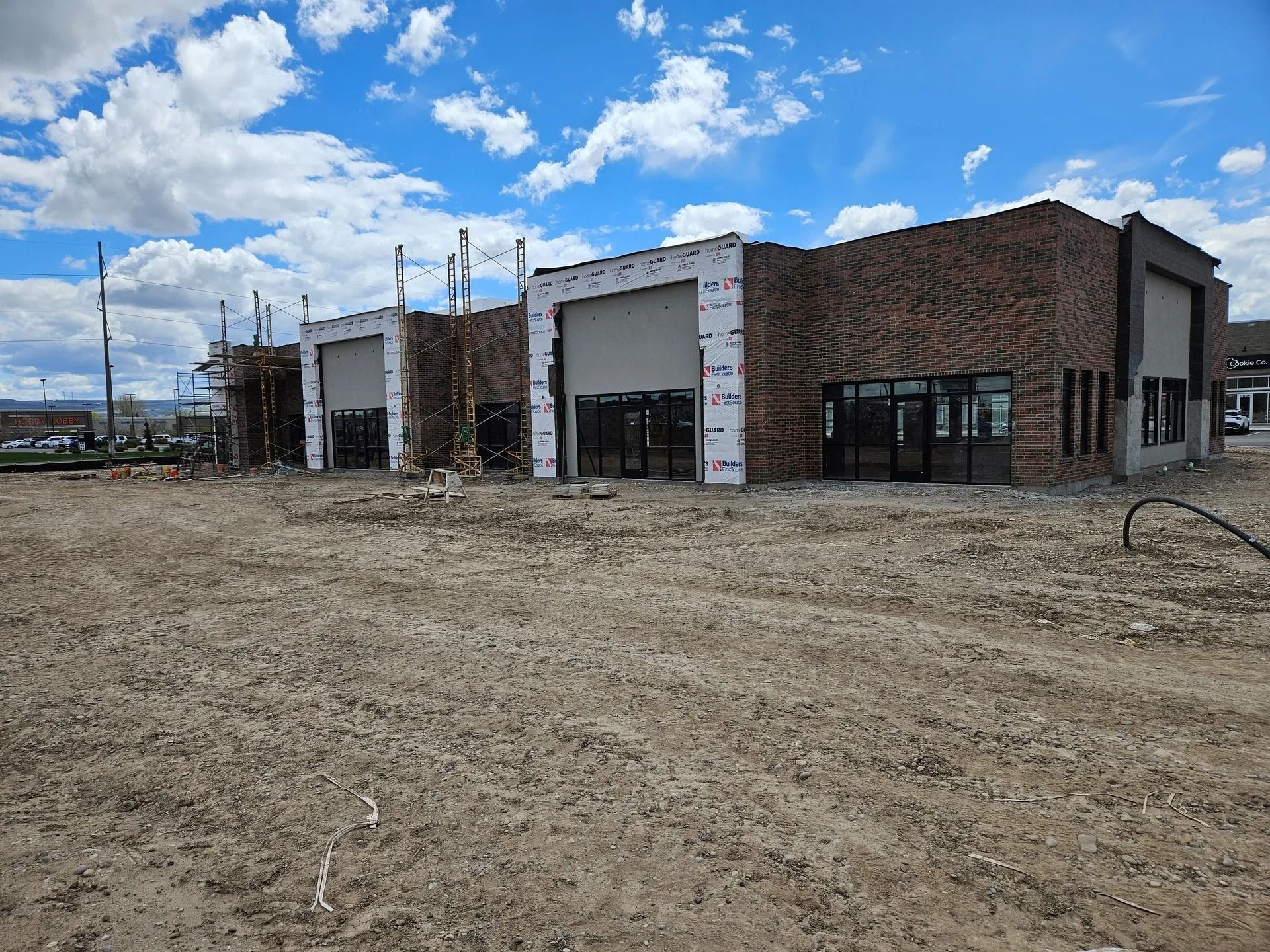 Construction site with brick building, garage doors, and windows, against a cloudy sky.