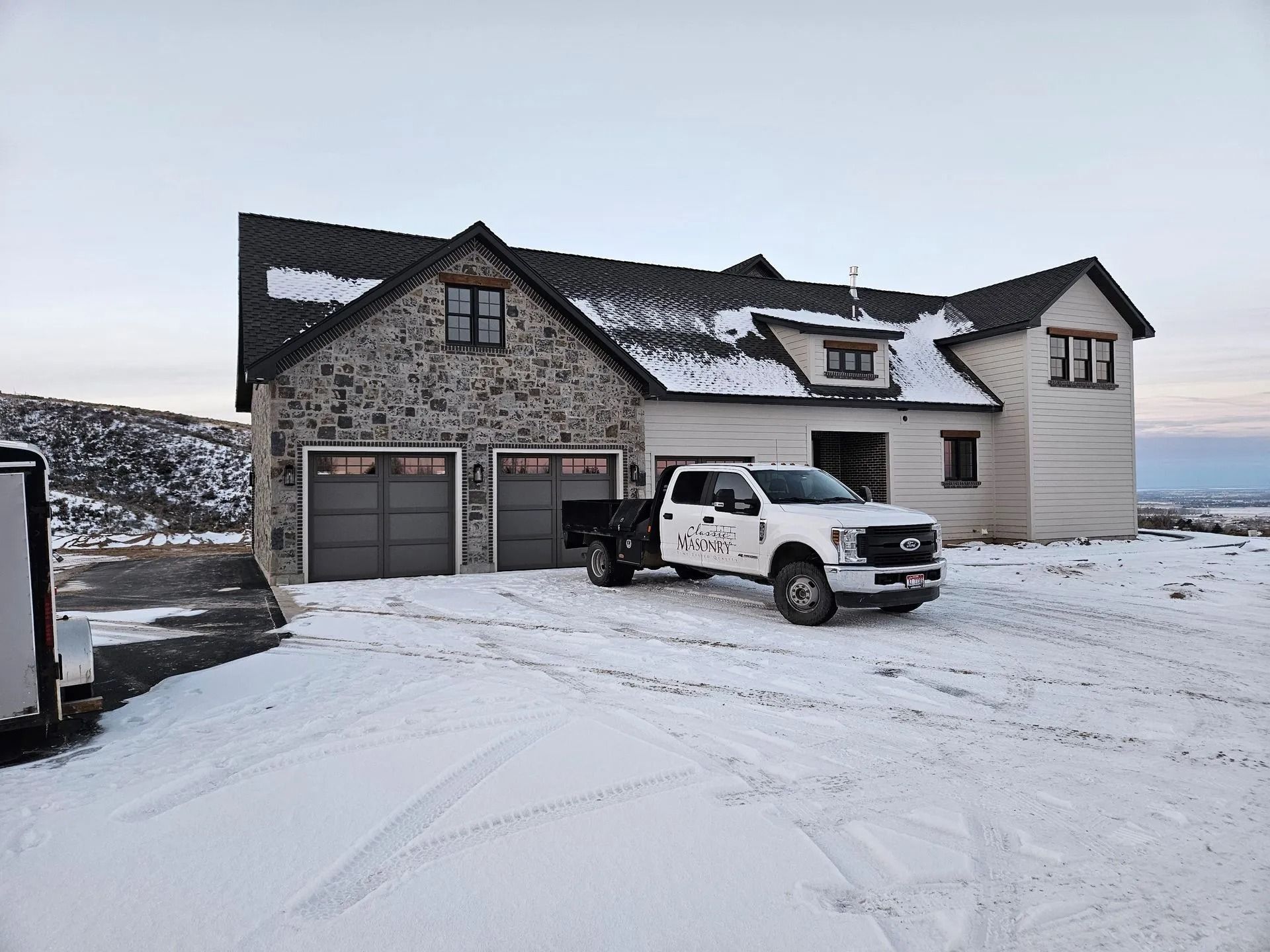 A snow-covered house with a pickup truck in front; snowy landscape and overcast sky.