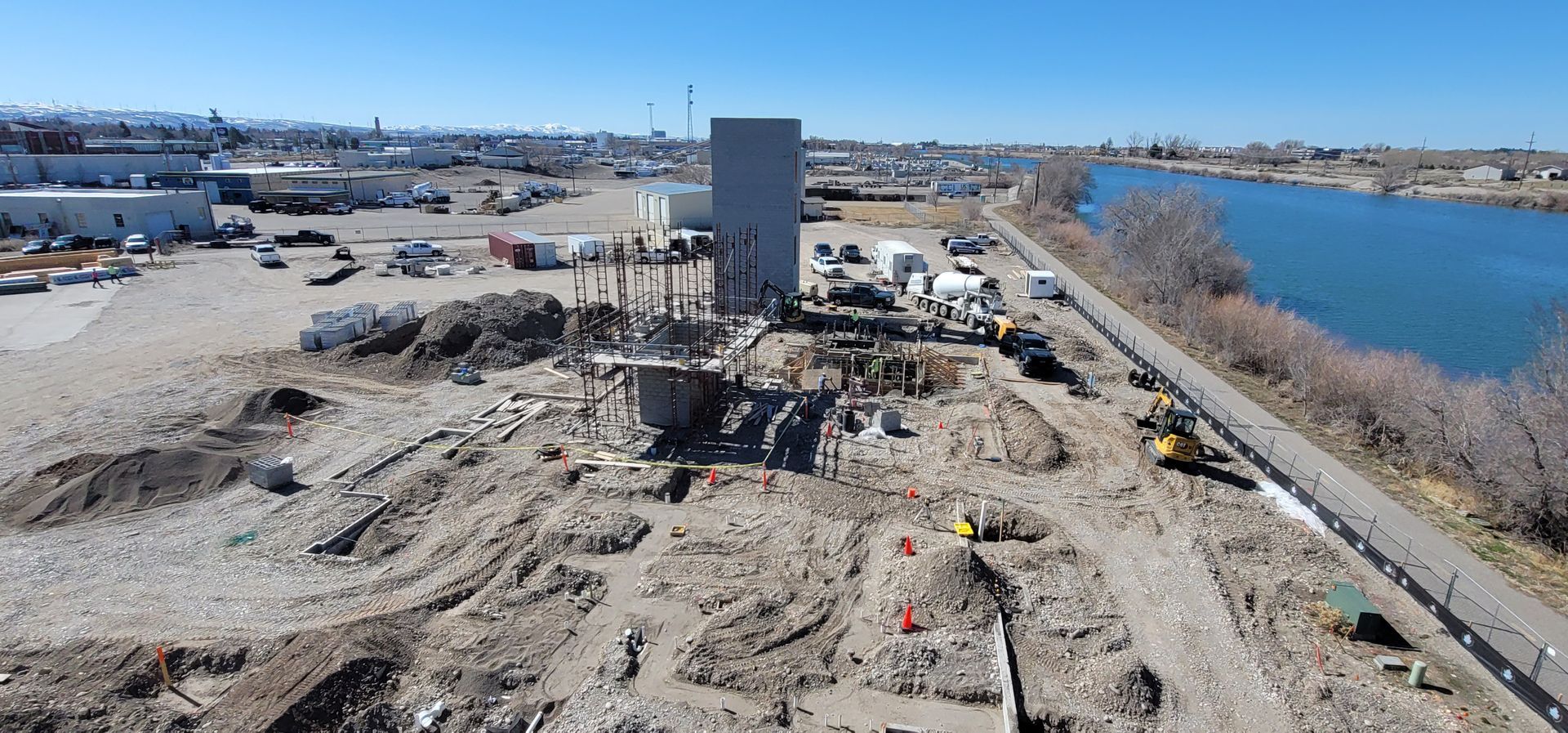 Construction site next to a river. A tall building stands amidst dirt and equipment.