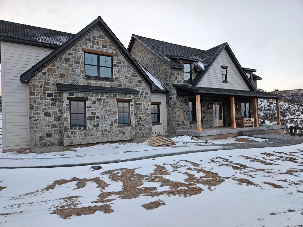 Two-story house with stone facade, snow-covered ground, and a covered porch with wooden pillars.
