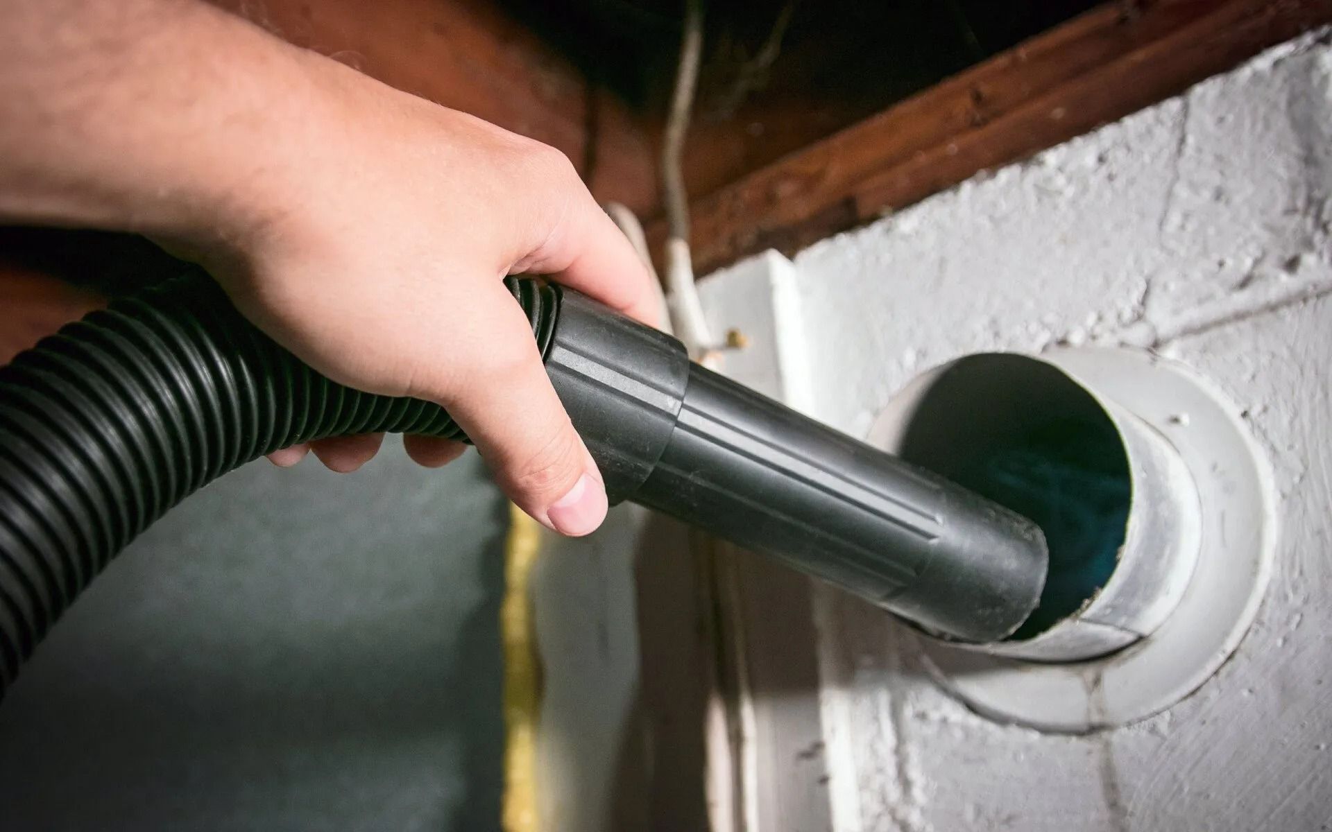Person vacuuming a white dryer vent in a basement.