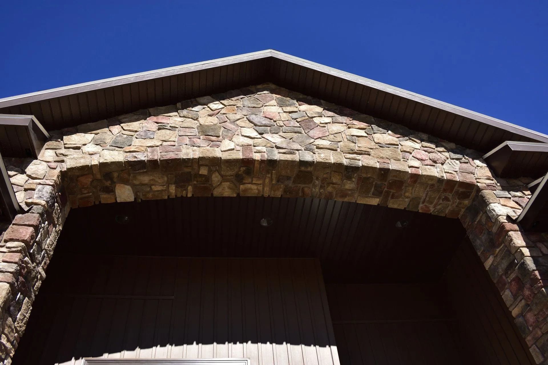 Stone archway entrance with brown siding under a clear blue sky.