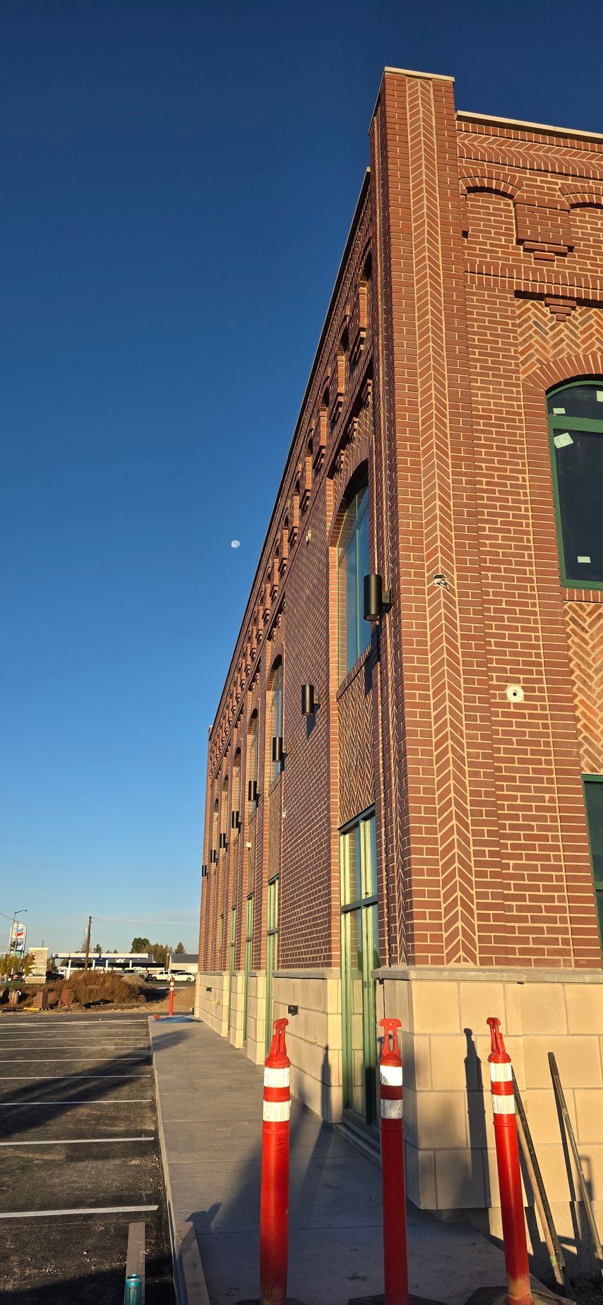 Brick building with red and white traffic cones in front, blue sky with a moon.