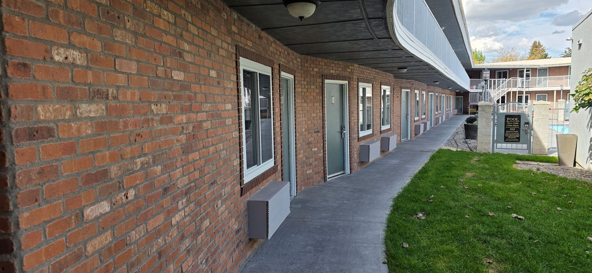 A brick building with a curved roof. A walkway and a patch of grass are in the foreground.