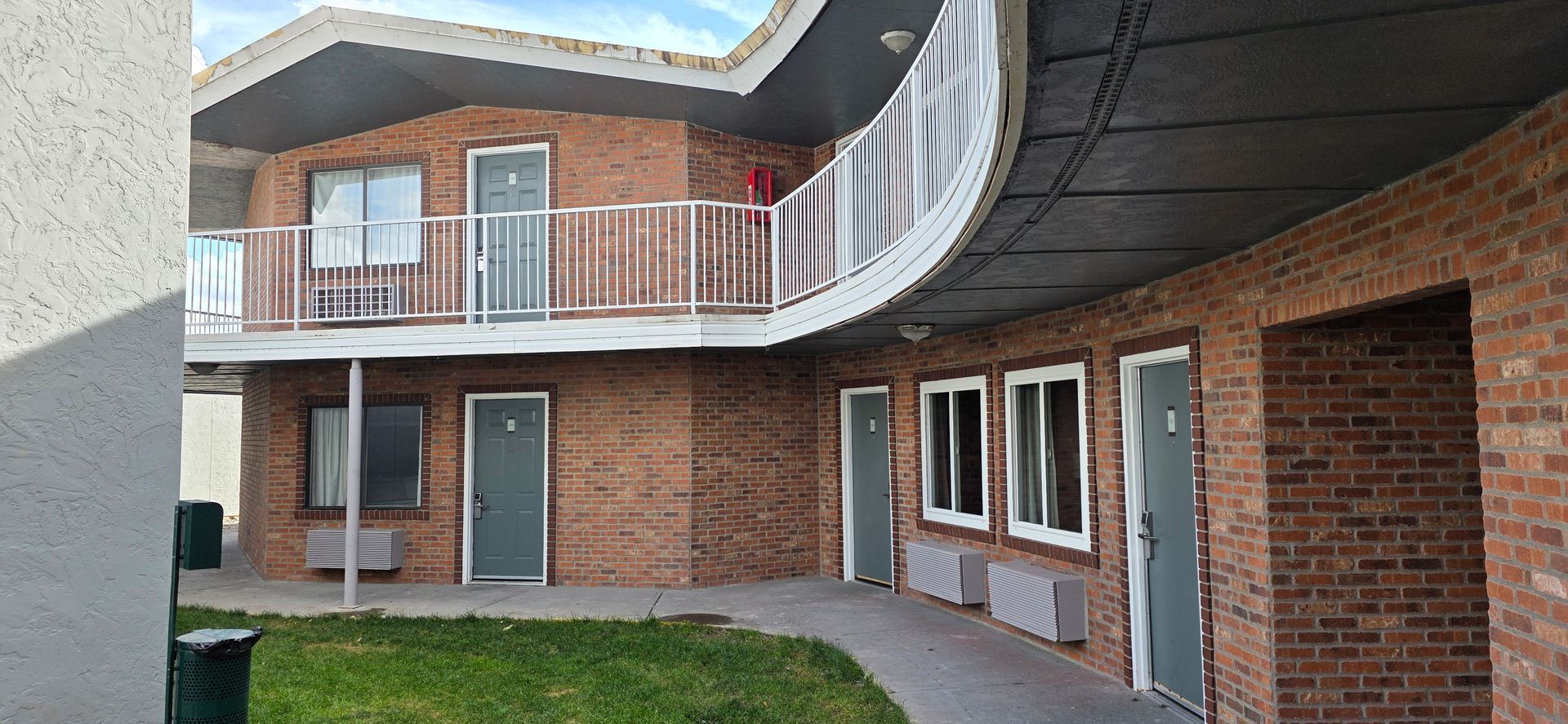 A two-story brick building with exterior doors and balcony, curved walkway on right.