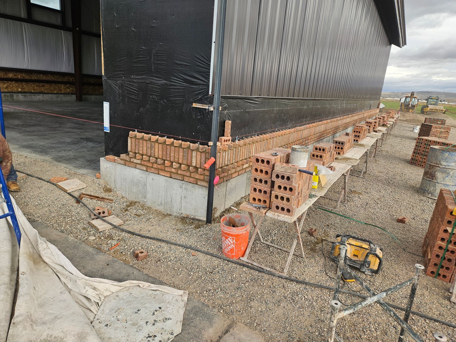 Construction of brickwork on a building's exterior. Bricks are laid on scaffolding, next to the concrete foundation.