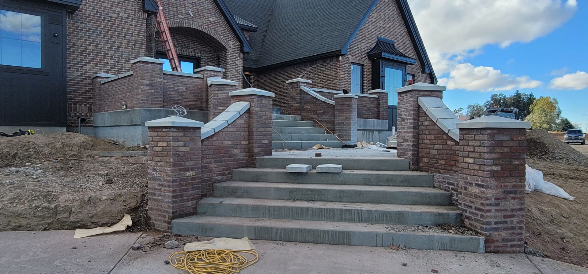 Brick home entrance with concrete stairs, brick pillars, and a partly cloudy sky.