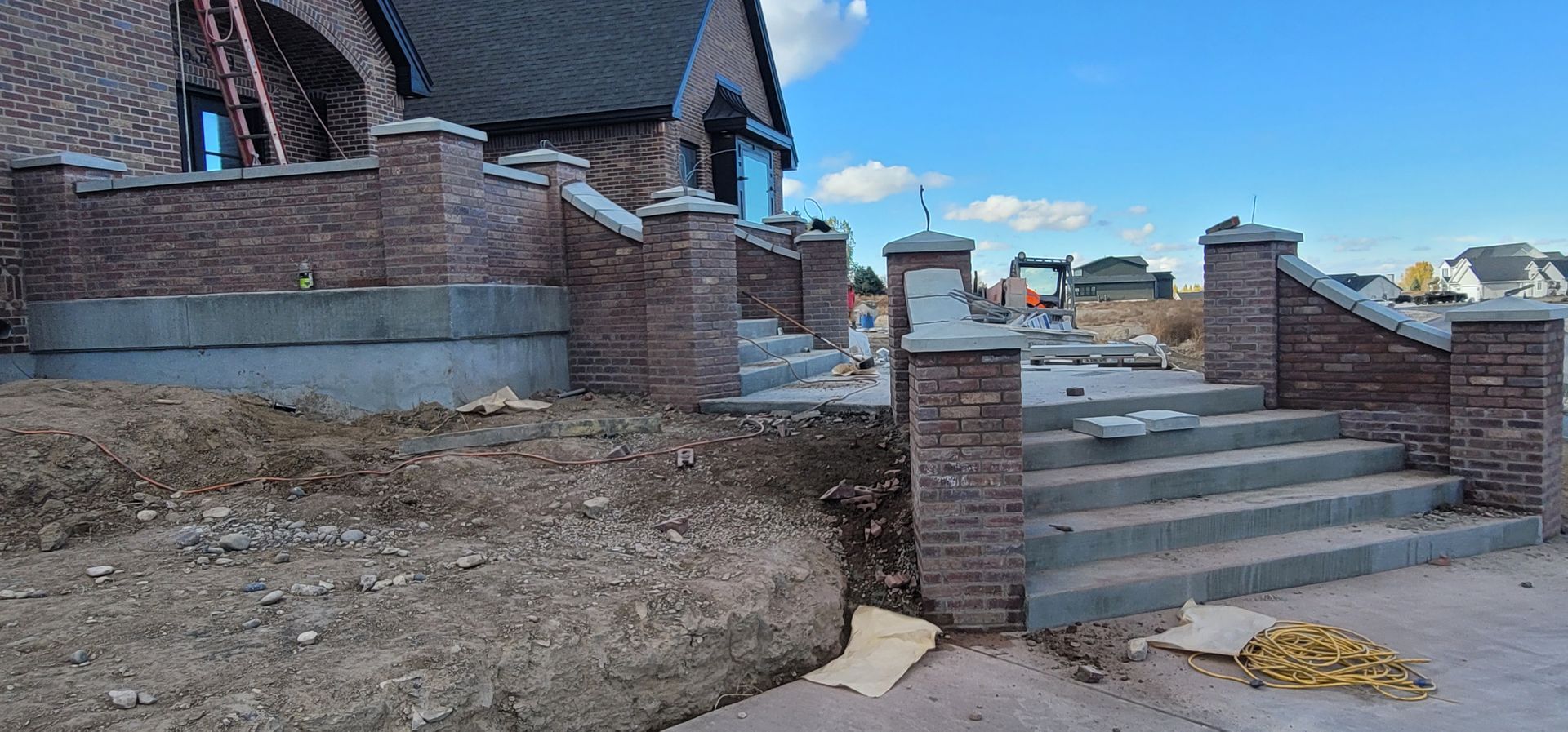 Exterior of a house under construction; brick pillars, concrete steps and exposed dirt.