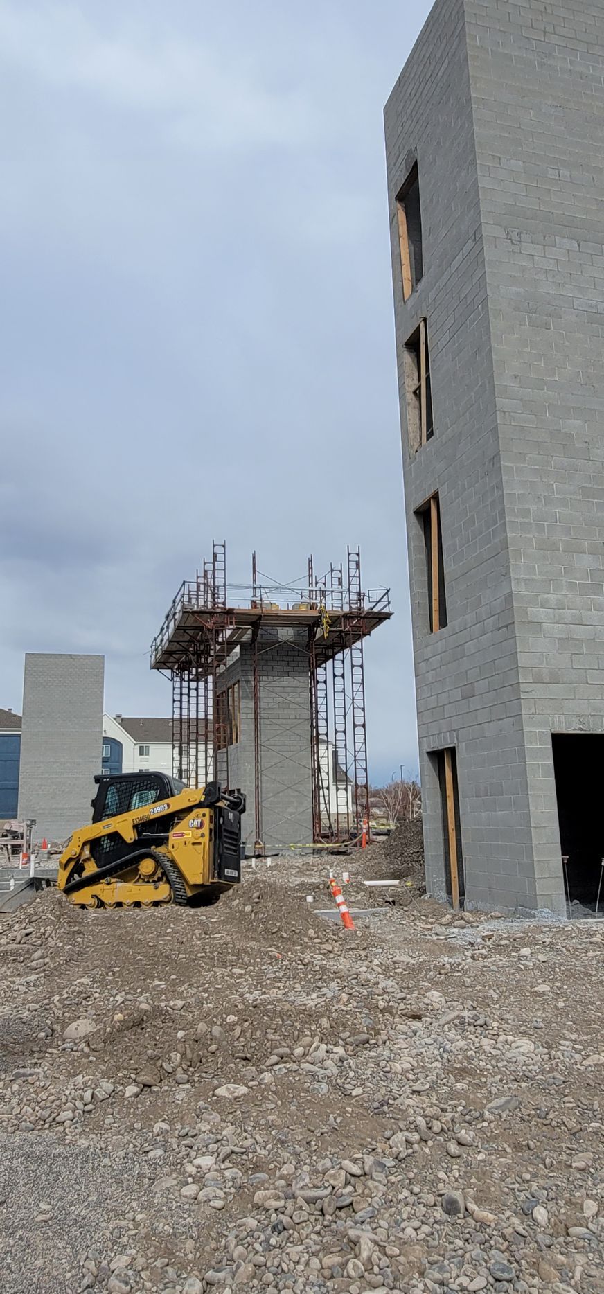 Yellow construction vehicle on a dirt pile; unfinished brick buildings in the background. Overcast sky.