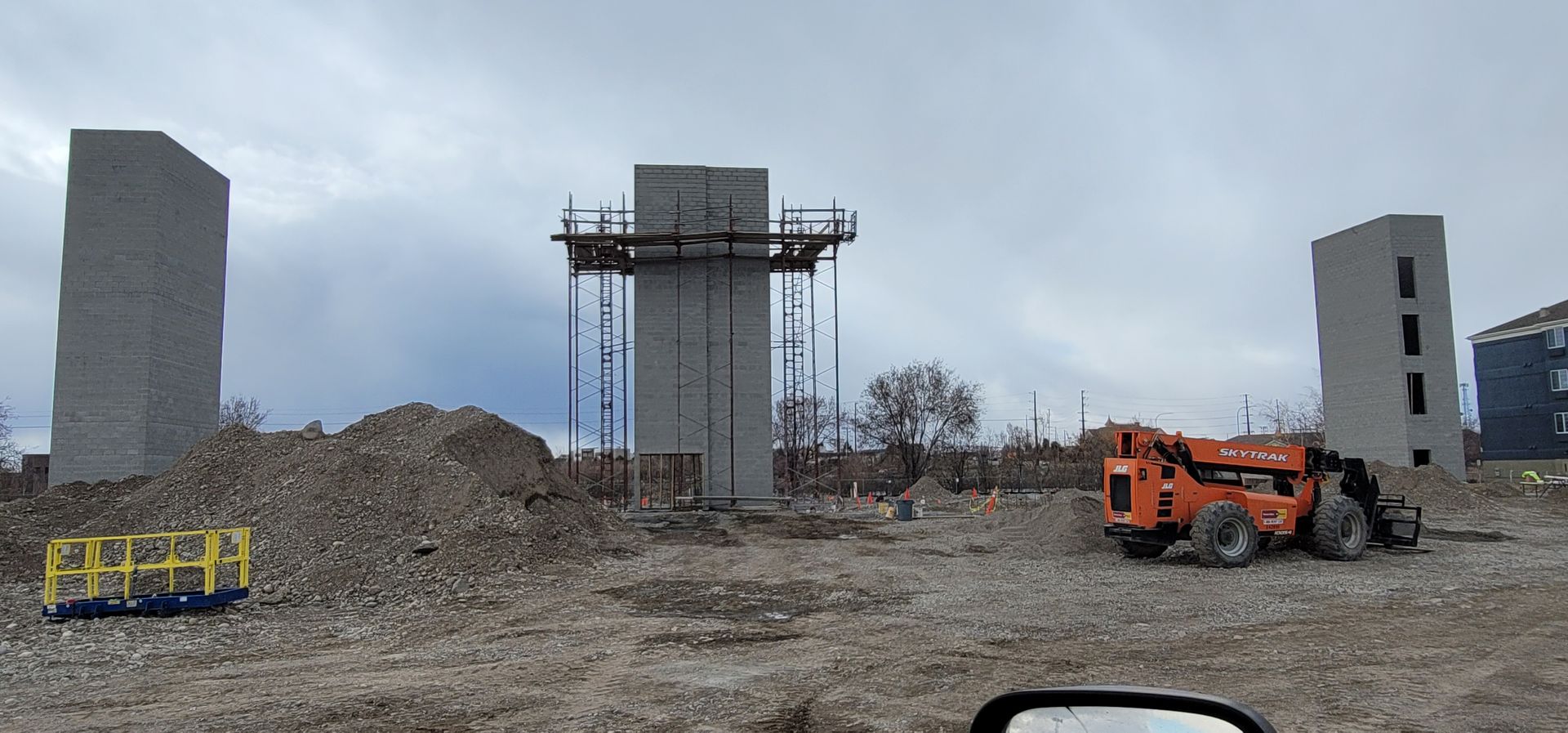 Construction site with concrete structures and a forklift against an overcast sky.