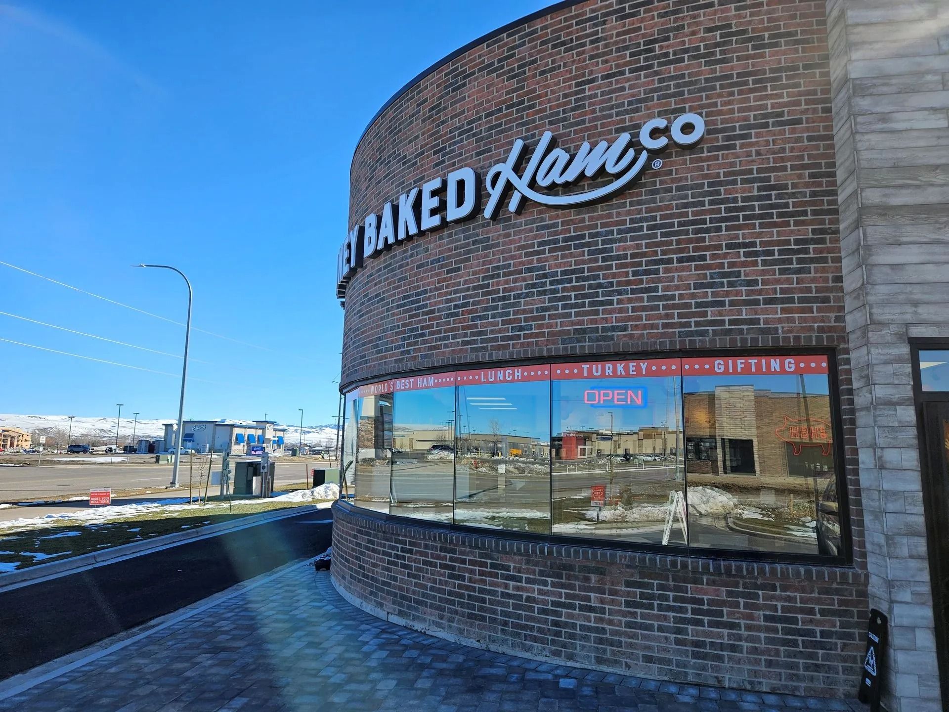 A brick building with the sign "Honey Baked Ham Co" and a curved glass window reflecting the surroundings.