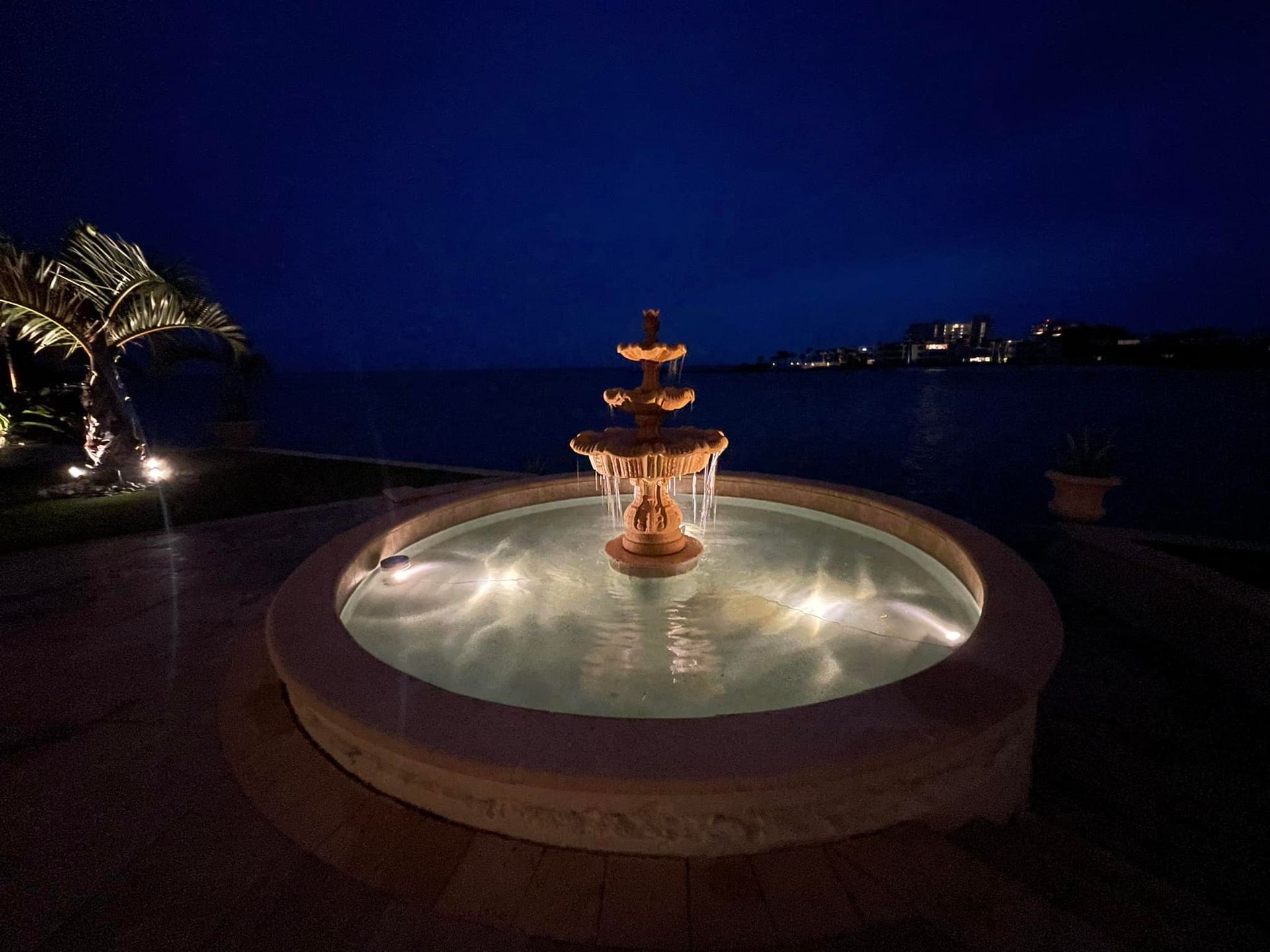 A fountain is lit up at night in front of a body of water