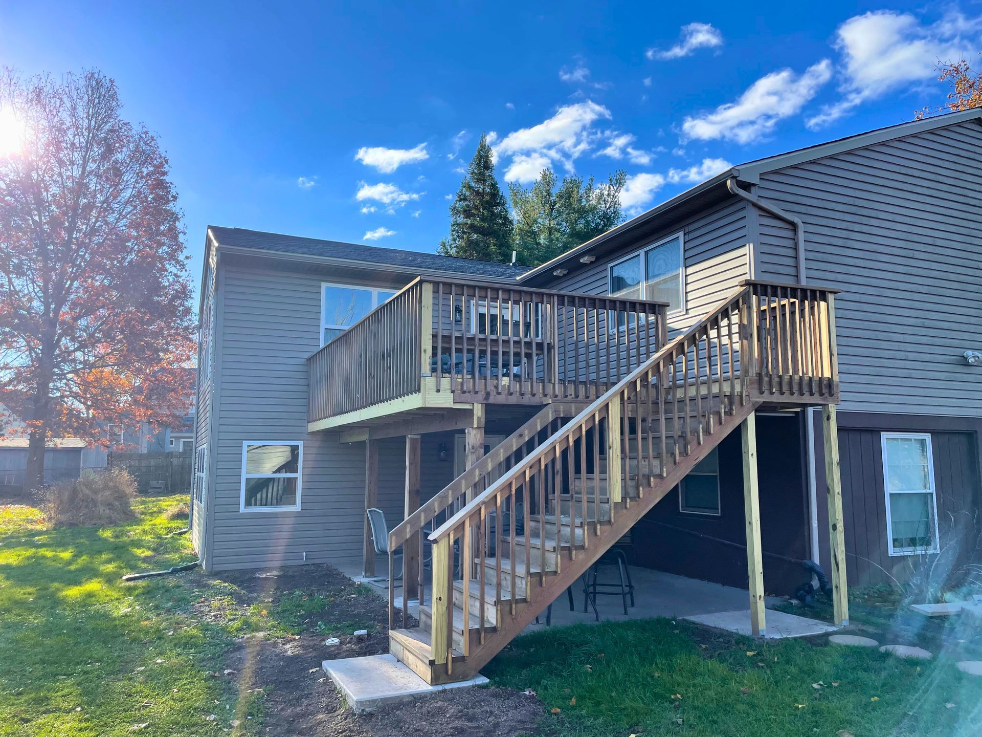 Two-story house with wooden decks and stairs. Brown siding, clear blue sky, and green grass.