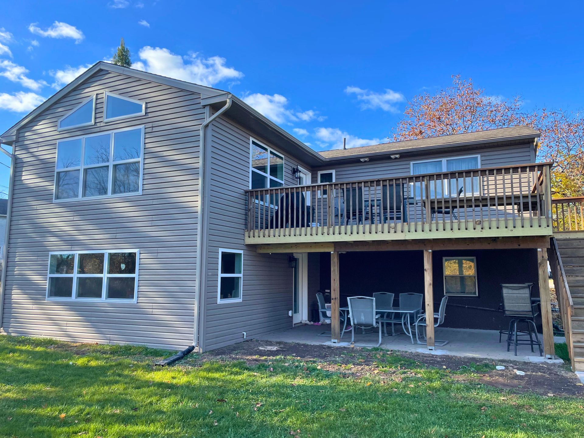 Back view of a two-story house with a large deck and a patio, brown siding, blue sky.