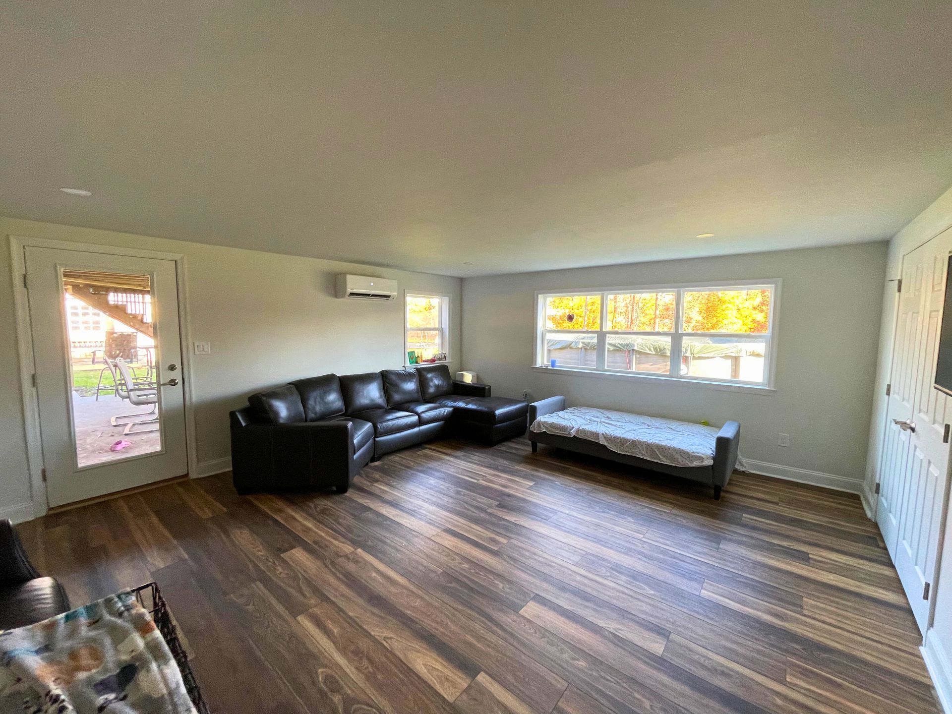 Living room with dark leather sectional, dog bed by window, and wood flooring.