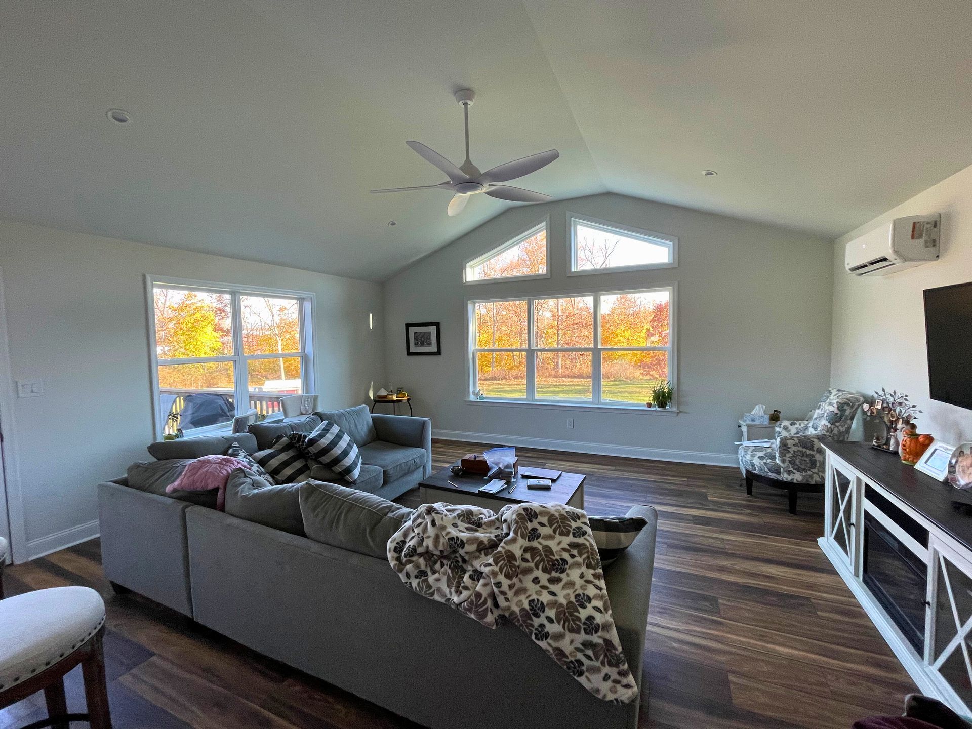 Spacious living room with gray sectional, windows framing fall foliage, and a fireplace.