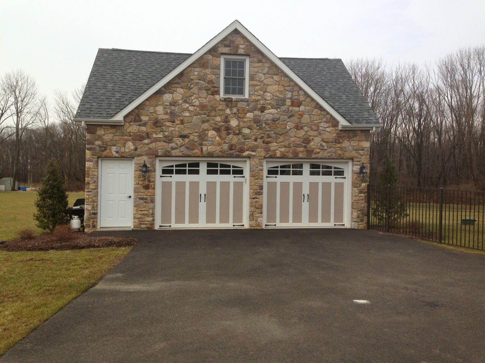 Stone garage with two white doors, small side door, and asphalt driveway.