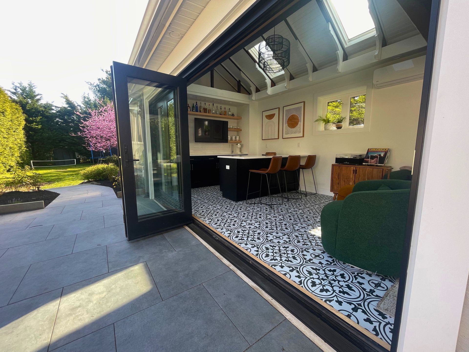 Open doors reveal a modern room with a black island, patterned floor, and green sofa, opening to a patio.
