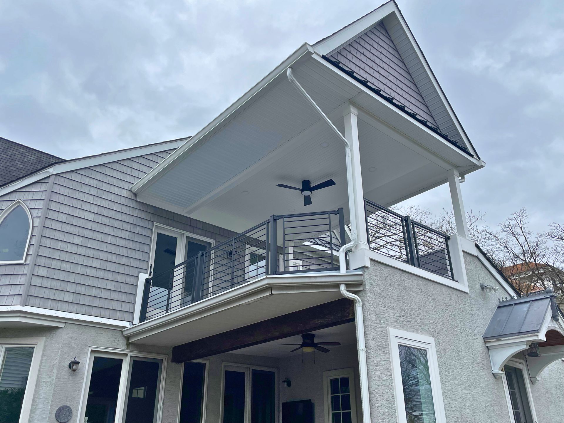 Two-story home with gray siding, a covered upper deck, and a lower patio; cloudy sky.