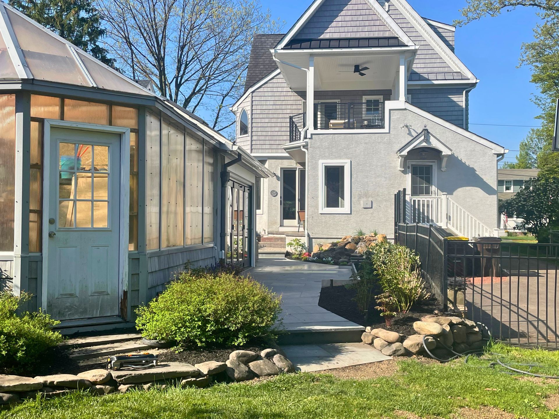 Backyard with a greenhouse, gray house, and stone landscaping.