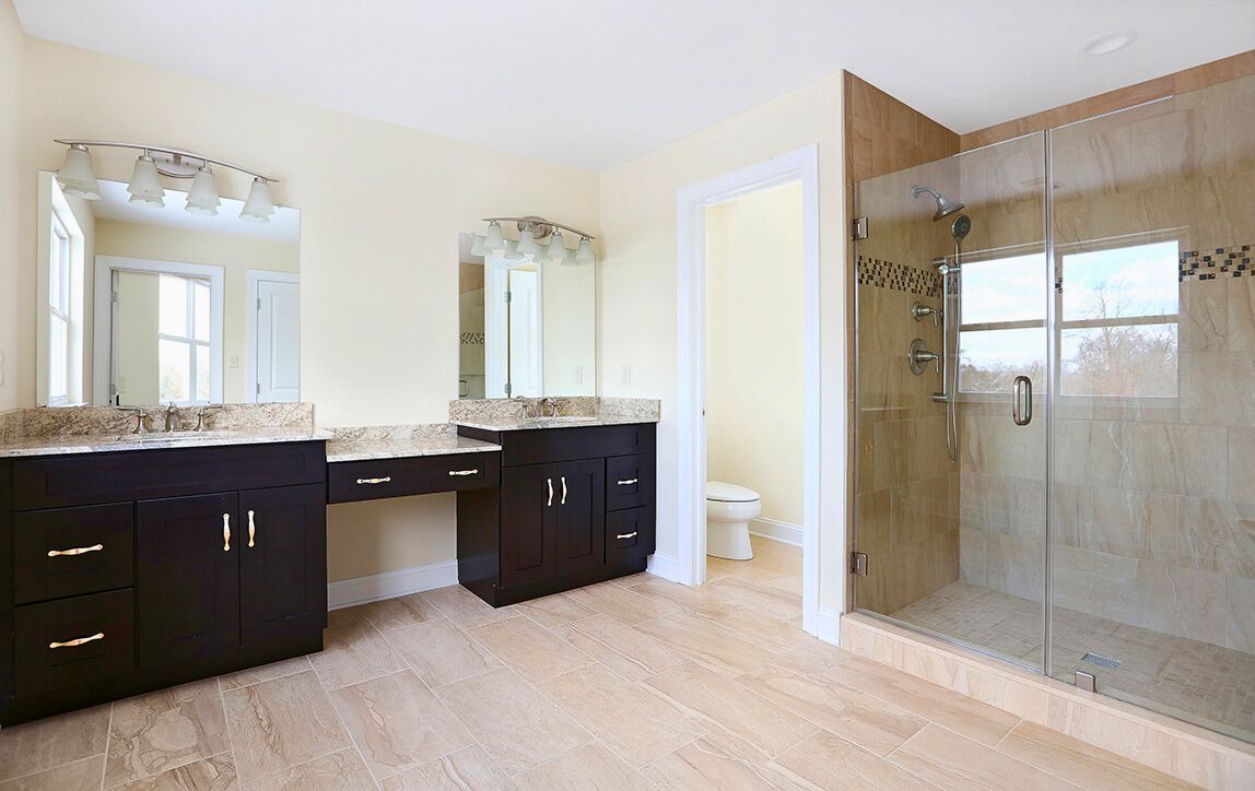 Spacious bathroom with dark wood vanities, glass shower, light-colored tile, and two mirrors.