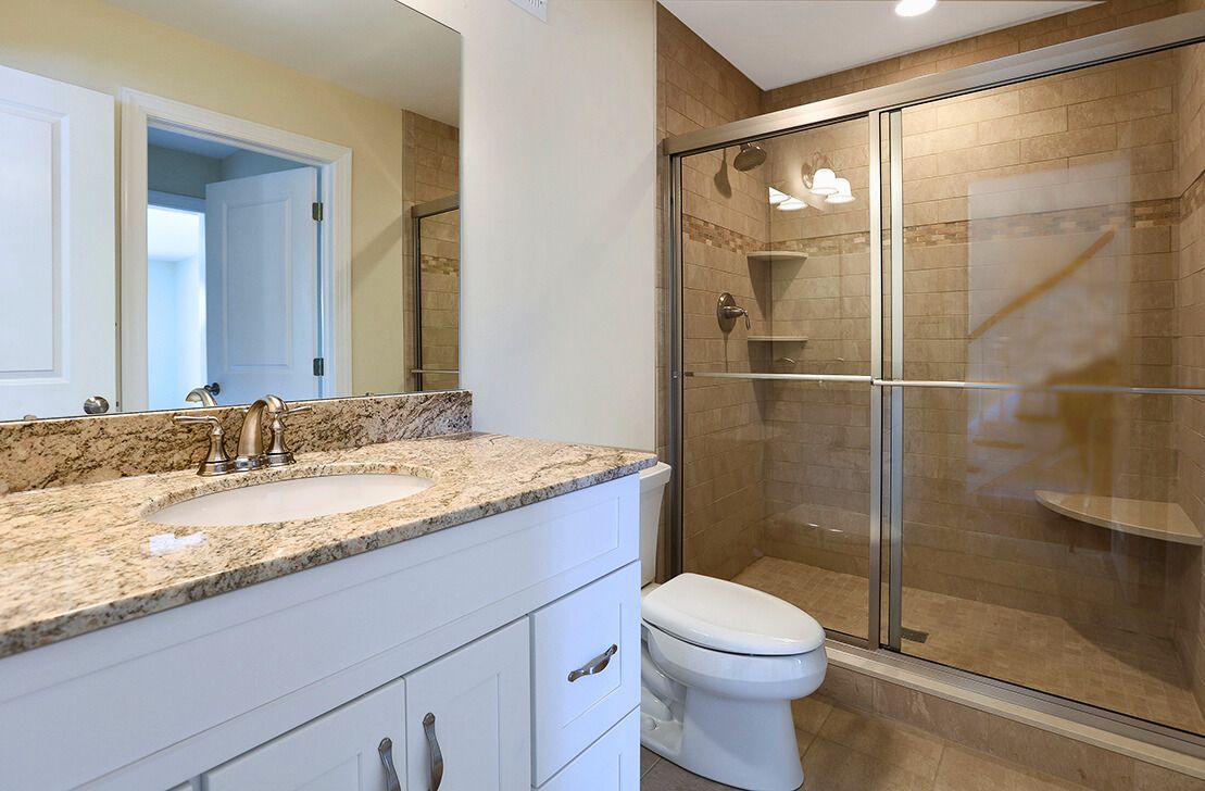 Bathroom with white vanity, granite countertop, glass shower, and beige tiled walls.