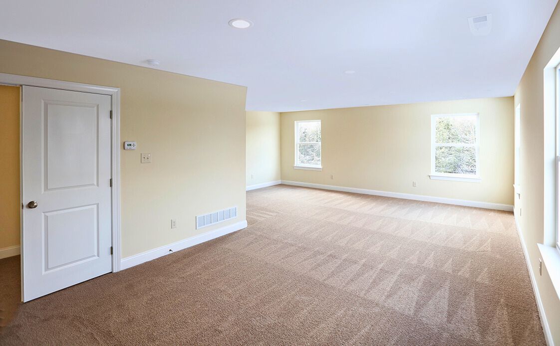 Empty room with tan carpet, beige walls, white door and trim, and two windows.