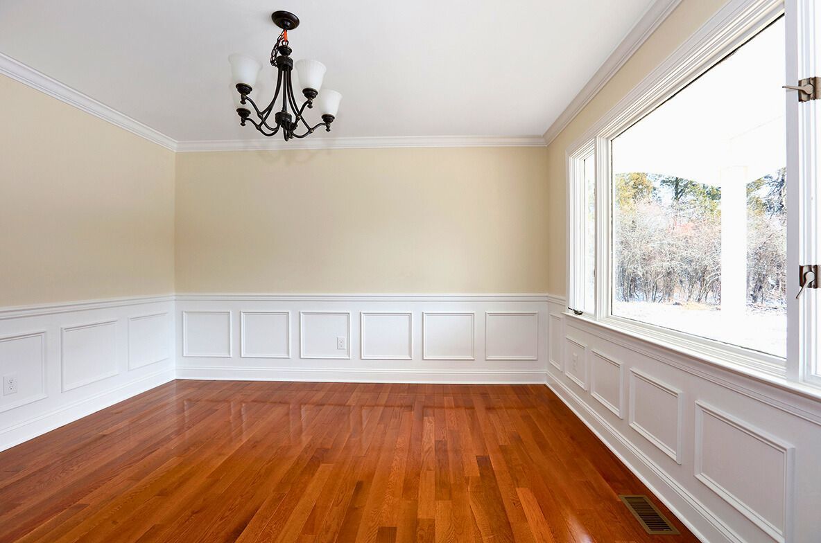 Empty dining room with hardwood floors, paneled wainscoting, large window, and chandelier.